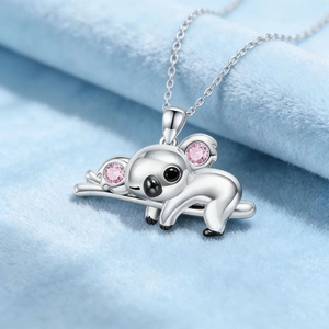 Collar con colgante de koala plateado y piedras rosas sobre fondo suave azul claro