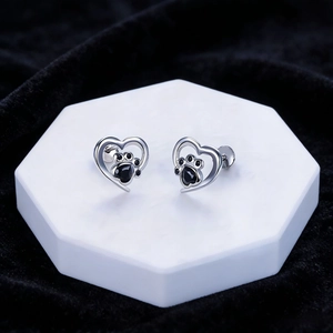 Detail of silver heart earrings featuring black gemstone cat paw prints on white display