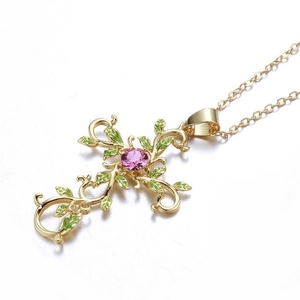 Exquisite gold cross necklace detail with pink gemstone and green enamel vine leaves