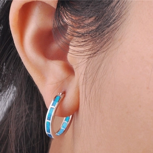 Close-up of classic silver hoop earrings featuring vibrant blue fire opal inlay on ears