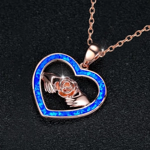 Rose gold heart necklace featuring a blue opal stone and hands holding a rose pendant