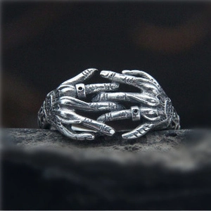 Detailed view of silver gothic ring featuring two interlocking hands on dark rock