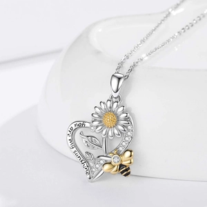 Macro-opname van zilveren harthalsketting met zonnebloem, bij en 'you are my sunshine' gravure