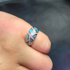 Detalle de un anillo geométrico plateado con ópalo azul y detalles de circón