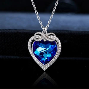 Blue heart crystal necklace with silver bow and diamond accents on black background