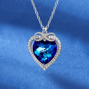 Blue crystal heart necklace with diamond-set infinity knot and bow on silk fabric