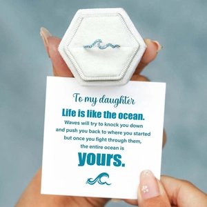 Close-up of wave-shaped silver ring with blue stones, velvet box, and a gift card