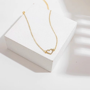 Collar minimalista de oro con colgante de corazón y cristales sobre pedestal blanco