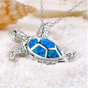 Detail of silver turtle pendant with blue opal inlay on a sandy beach background