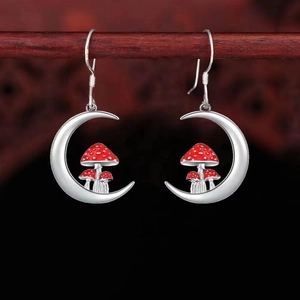 Detailed close-up of crescent moon earrings with red mushroom motif on a wooden stand