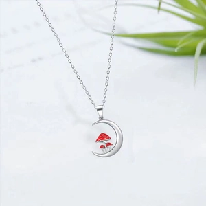 Detailed shot of a silver crescent moon necklace with small red mushroom charms on white paper