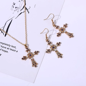 Détail d'une parure de bijoux croix dorée vintage avec strass violets et accents blancs