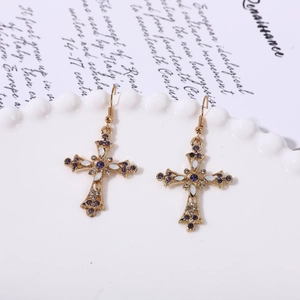 Détail de boucles d'oreilles croix dorées vintage avec strass violets et émail blanc