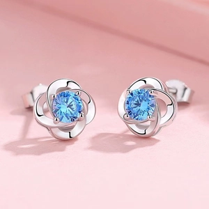 Detail of flower stud earrings with four-petal silver design and blue round gemstone