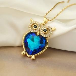 Schattige gouden uil hanger met blauw hartvormig kristal op witte zijden achtergrond