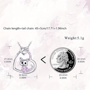 Cute silver heart pendant necklace with pink gem and cat charm next to coin for scale