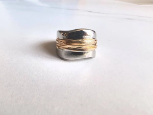 Détail macro d'une bague large ondulée avec base argentée et fil d'or torsadé