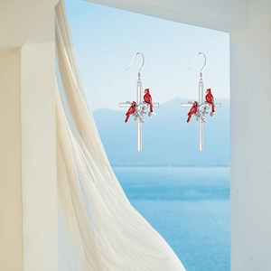 Cross earrings with cardinal birds and green leaves design in a scenic coastal view