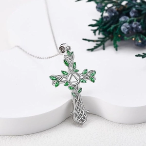 Cross pendant necklace with green enamel tree of life leaves on a white stand