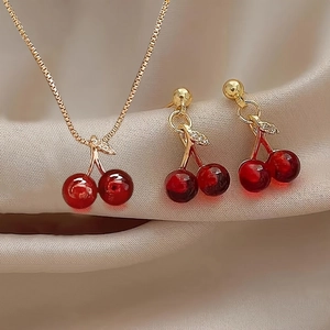 Elegant red cherry jewelry set featuring a gold necklace and stud earrings on silk