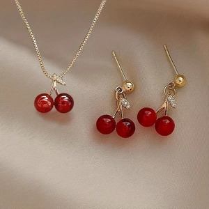 Creative red cherry jewelry set with necklace and earrings on champagne silk background