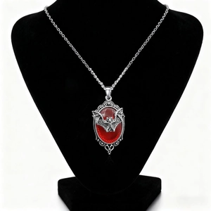 Gothic vampire bat necklace with large red gemstone pendant on a black bust display