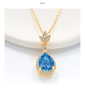 Macro di una collana d'oro con gemma blu a goccia e dettagli in foglia di diamanti