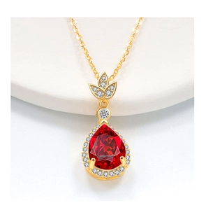Macro di una collana a goccia in oro con gemma rossa sfaccettata e foglie di zircone
