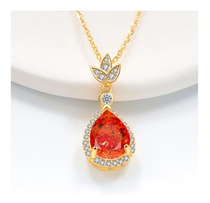 Macro di una collana in oro con una gemma arancione a goccia e dettagli di foglie