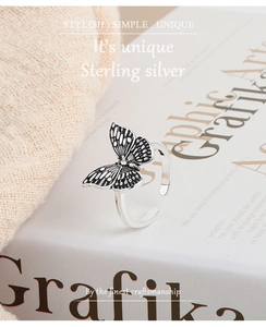 Silver butterfly open ring with vintage black etched details on beige knit and book