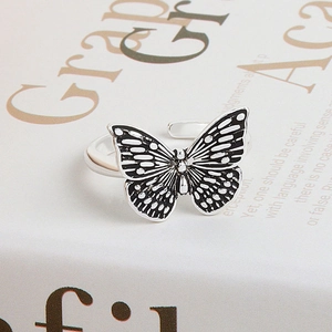 Elegant silver butterfly open ring with black enamel details on a book background