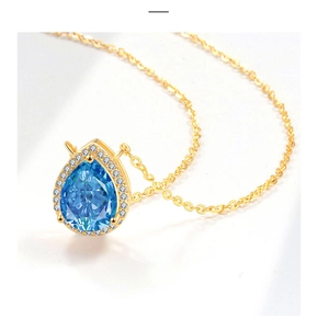 Macro detail of a pear-cut blue gemstone necklace with halo setting and gold chain
