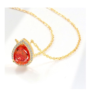 Macro detail of pear-cut orange gemstone pendant with white diamond halo on gold chain