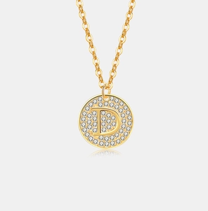 Detail van een ronde gouden hanger met letter D en glinsterende kristallen op een O-ketting