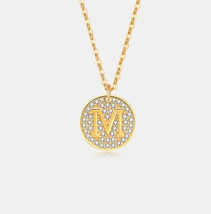 Detail van de gouden ronde hanger ketting met letter M en zirkonia steen plaveisel