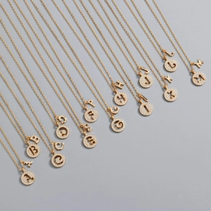 Macro detail of gold-plated circular pendants with micro-inlaid zircons and letter charms