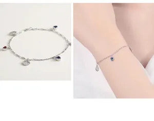Détail du bracelet S925 en argent avec cœur, gemmes bleues et breloque coquillage sur poignet
