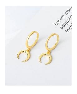 Macro view of gold hoop earrings featuring crescent moon pendants on textured paper