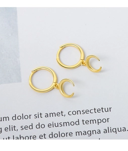 Detail of gold crescent moon dangle earrings on a minimalist white background