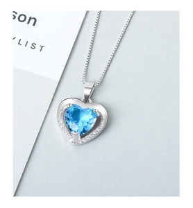 Close-up of a silver heart necklace featuring a blue gemstone and white zircon halo