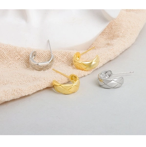Detailed view of silver and gold C-shaped earrings with quilted diamond pattern