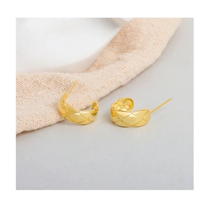 Detailed view of gold rhombic textured C-shaped earrings on beige fabric background