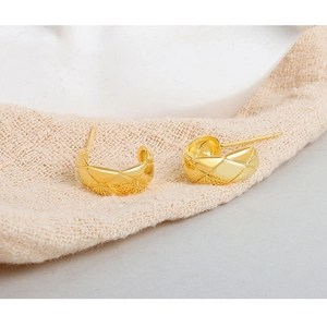 Detail of gold-plated geometric quilted pattern half-hoop earrings on neutral fabric