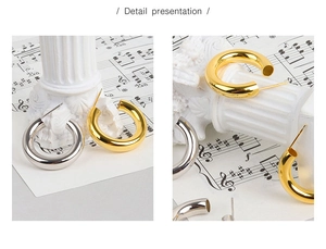 Detailansicht dicker C-förmiger Ohrstecker in Gold und Silber auf Notenblättern