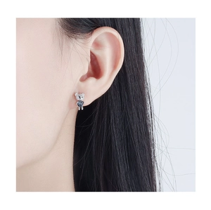 Detail of silver bear stud earring with heart-shaped blue stone on model's ear
