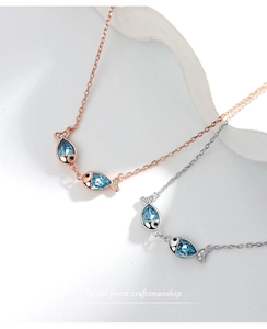 Detailed macro of two kissing fish necklaces with blue teardrop crystals and fine zircons