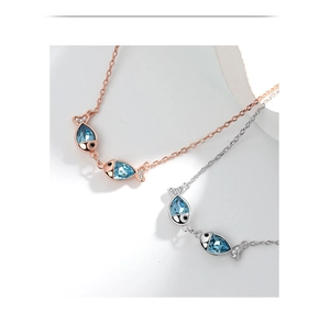 Detailed close-up of kissing fish necklaces with blue crystals in silver and rose gold