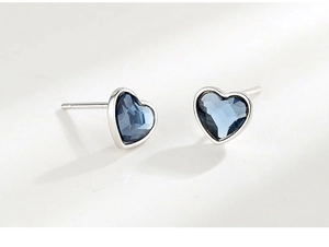 Close-up of heart-shaped silver earrings featuring faceted blue crystals and polished finish