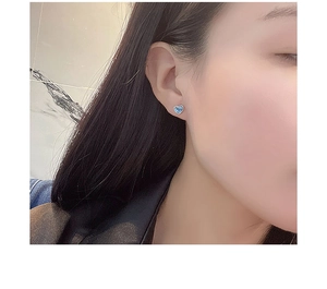 Close-up of a model wearing a heart-shaped stud earring with a blue opal stone