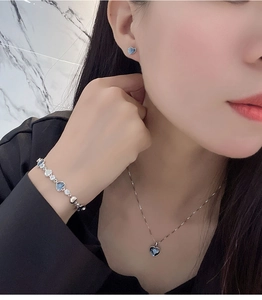 Detailed view of silver heart jewelry set with blue stones worn by model on neck and wrist